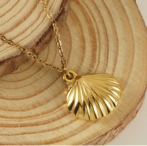 Detailed view of a polished gold seashell pendant necklace on a natural wooden block