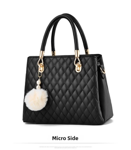Detail of elegant black quilted handbag with plush pompom and pearl charm on white background