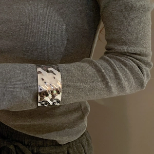 Close-up of wide silver hammered metal cuff bracelet worn over a gray knit sleeve