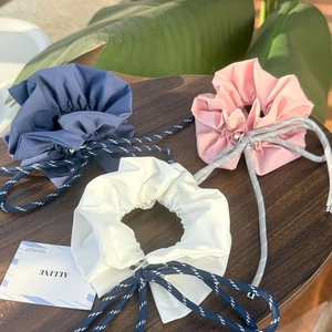 Three colorful scrunchies with woven drawstring details on a dark wooden surface