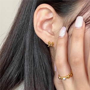 Close-up of elegant gold bow earrings and heart ring set on female model's ear and finger