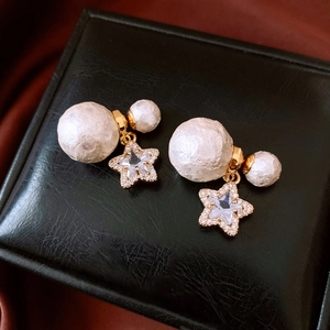 Detail of 18K gold plated pearl earrings with zircon star charms on black leather