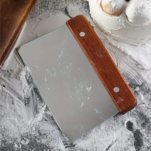 Stainless steel dough scraper with wooden handle on a flour-dusted baking surface