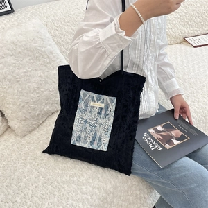 Détail d'un sac cabas en velours noir avec un écusson en dentelle bleue et anses