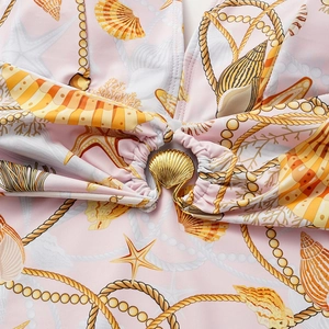 Detail of seashell print swimwear featuring a gold shell-shaped metal clasp on soft pink fabric