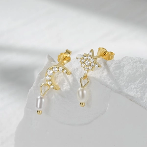 Detail of asymmetric gold star and moon stud earrings with white pearls on white rock