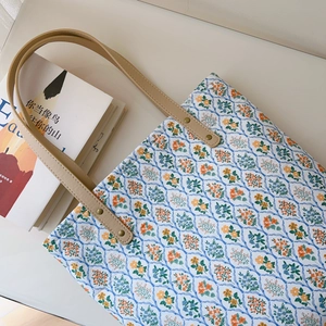 Detail of floral canvas tote bag with metal rivets and leather handles on white table