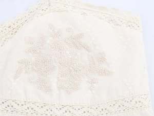 Détail de la broderie blanche et de la bordure en dentelle sur le tissu du vêtement