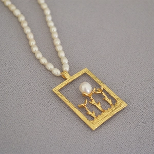 Macro detail of rectangle gold pendant with floral craft and rice pearl chain