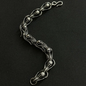 Detail of silver skull and cobra dragon bone bracelet with S-hook on dark background