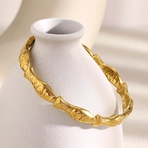 18K gold plated stainless steel cuff bracelet with fish scale texture on a ceramic vase
