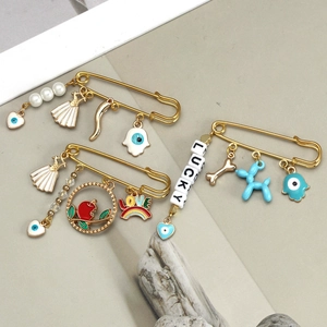 Detail view of gold safety pins with evil eye, pearl, and colorful charms for clothing