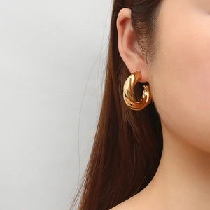 Elegant gold twisted C-shaped hollow earrings shown on model with polished metallic finish