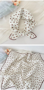 Detailed macro view of cream square silk scarf with brown heart pattern and stitched edges