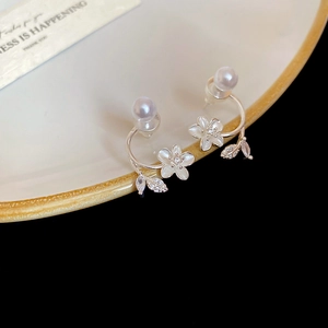 Detail of silver stud earrings with white flower, pearl, and crystal leaf on ceramic tray