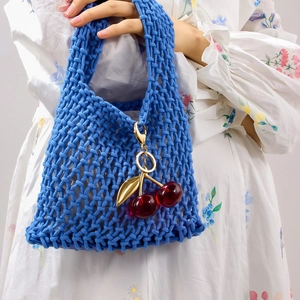 Blaue geflochtene Handtasche mit rotem Kirsch-Anhänger aus Harz in Sommeratmosphäre