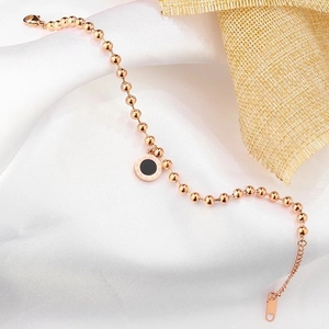 Close-up of rose gold bead bracelet with black roman numeral disc on silk and burlap