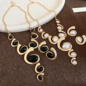Detail of two gold metal fringe necklaces with black and pearl oval stones on display