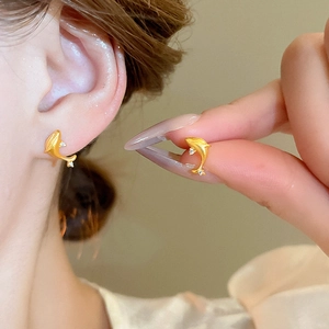 Close-up of golden dolphin earrings with small diamonds shown on ear and in hand