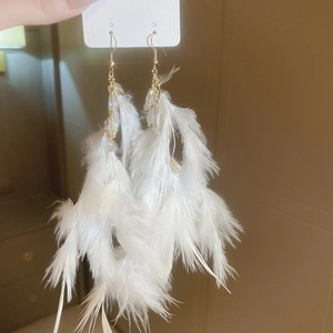 Detail of white feather tassel earrings with gold hooks and beads on a display card