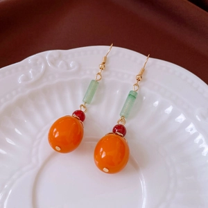 Detailed close-up of retro Chinese style persimmon drop earrings on a white ceramic plate