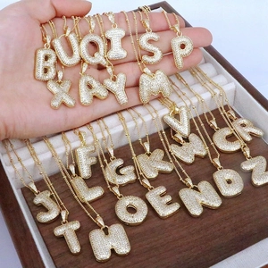 Gold letter pendant necklace with cubic zirconia pave settings on wooden tray