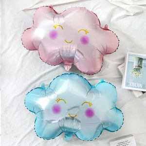 Close-up of pink and blue smiling cloud foil balloons with rainbow tassels on white fabric