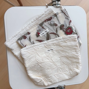 Three-piece floral and embroidered linen pouches set on a white chair in a minimalist style
