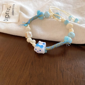Detail of handmade ceramic cat bead on a woven blue and white cord bracelet