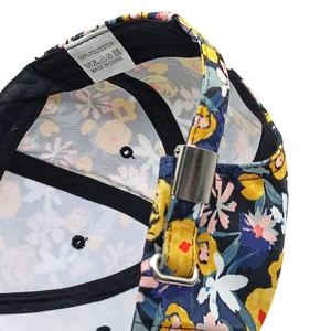 Détail de casquette fleurie montrant la boucle en métal et l'étiquette 100% polyester