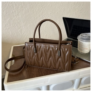 Brown quilted PU leather handbag on white stool with laptop in a lifestyle office setting