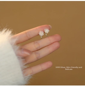 Detail of S999 sterling silver rose earrings held between fingers with soft lighting