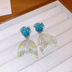 Gros plan de boucles d'oreilles fleurs bleues et queue de poisson sur plateau de velours