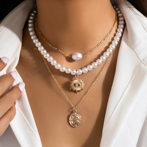 Close-up of layered gold necklace set with star, pearl, and textured coin pendants on model