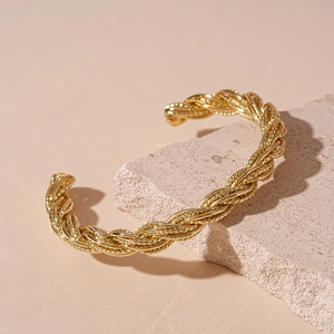 Detailed close-up of a gold twisted rope cuff bracelet on a natural stone surface