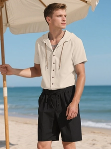 Linen set featuring beige hooded button shirt and black drawstring shorts on the beach
