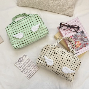 Close-up of dot-patterned travel bags featuring 3D white wing decorations on canvas fabric