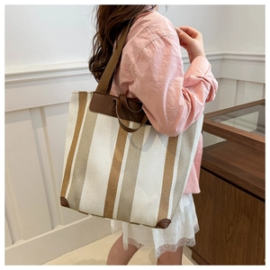 Close-up of striped canvas tote bag showing leather corner and wide shoulder strap detail