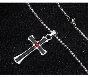 Detail of silver cross pendant with red gemstone and black inlay on a box chain