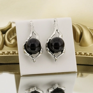 Detail of silver wavy earrings featuring a black pearl on a white display card with reflection