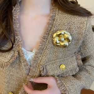 Golden camellia flower brooch with matte metal finish on brown tweed jacket lapel