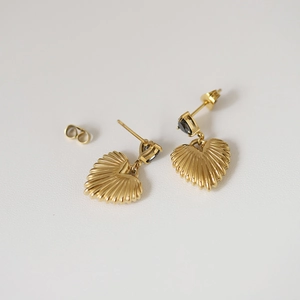 Macro detail of heart-shaped gold earring with shell texture and black gemstone inlay