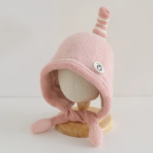 Detail of pink knitted baby hat featuring cute penguin patch and top twist decoration