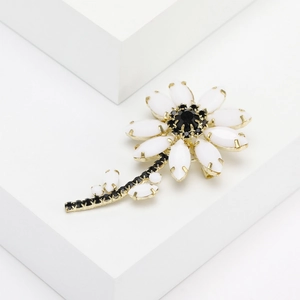 Elegant white daisy flower brooch with gold plating and black crystals on white pedestal
