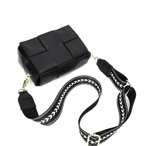 Detail of black woven leather bag with geometric patterned wide strap and gold hardware