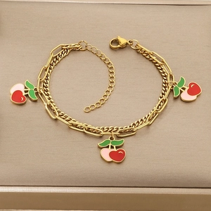 Detailed close-up of double-layer gold chain bracelet with red cherry pendants