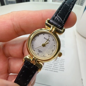 Close-up of a women's quartz watch with gold case, black leather strap, and diamond dial