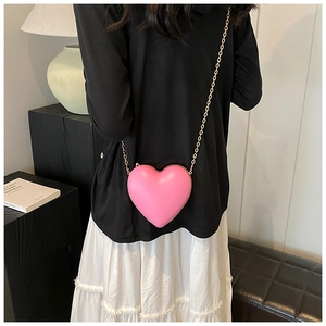 Detail of pink heart-shaped crossbody bag with gold chain strap on model shoulder