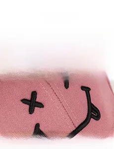 Gros plan sur la casquette en sergé rose avec broderie détaillée d'un visage souriant