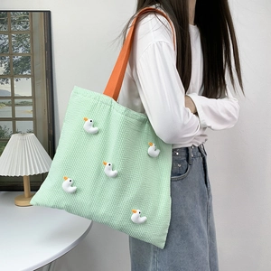 Close-up of green checkered canvas tote bag with 3D duck dolls and orange straps